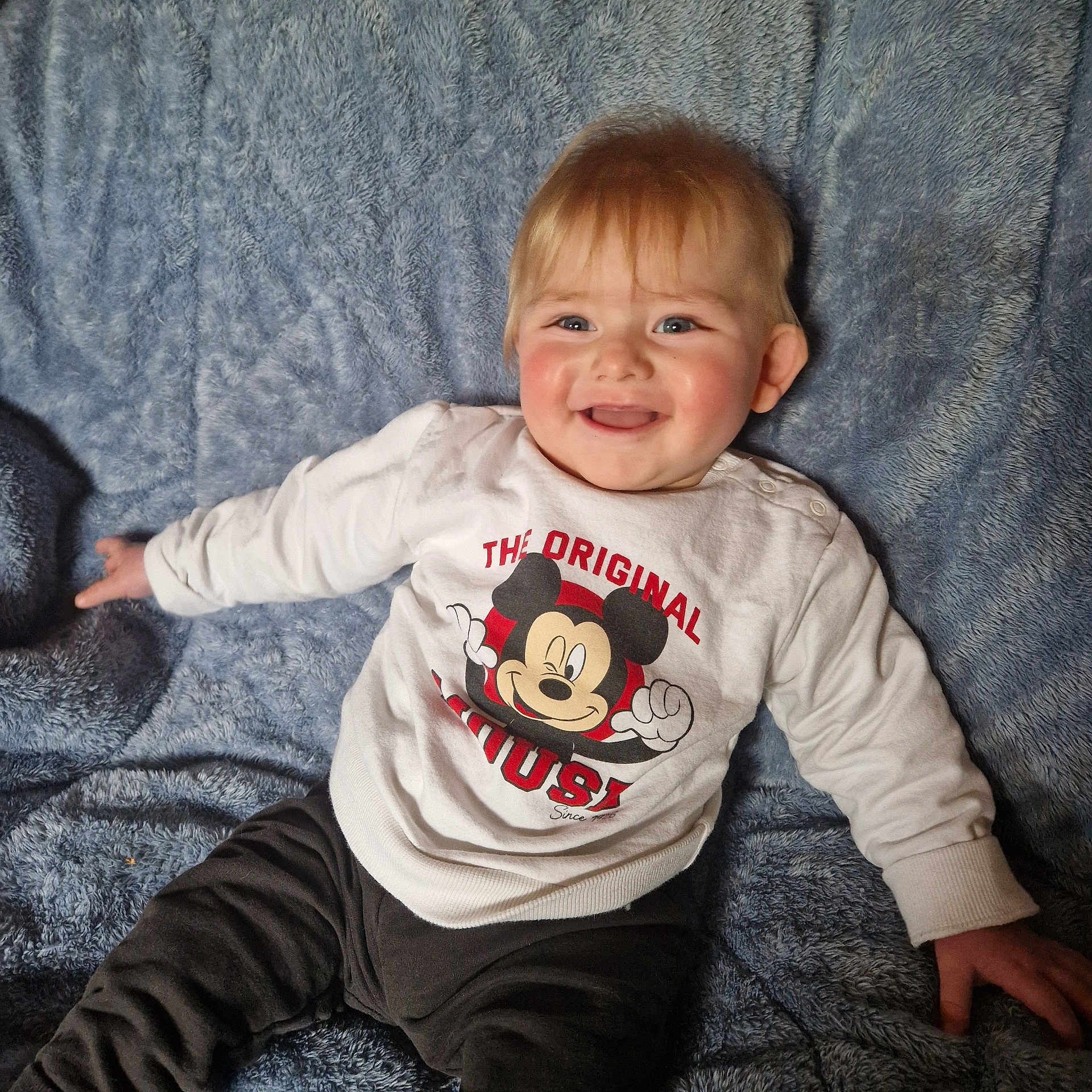Gabin a rejoint le concours — aidez-le/la à gagner de superbes lots ! baby, child, smiling, sitting, mickey_mouse, white_sweater, blue_blanket, happy, cute, infant, portrait, clothing, soft_texture, indoor, young_child, face, person, casual, comfort, playful