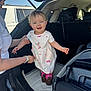 toddler, child, woman, car, car_trunk, dress, boots, smile, outdoor, daylight, person, vehicle, supporting_hand, baby, casual_clothing, happy, parent, transportation, stroller, sunlight