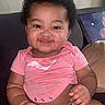 baby, child, smiling, corn, pink_shirt, diaper, couch, indoors, happy, messy_face, curly_hair, sitting, phone_screenshot, video_selected, user_interface, screen_capture, cute, infant, holding_food, casual_clothing