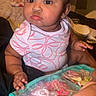 baby, child, girl, pink_bows, hair_accessories, pouch, hand, seated, curious, indoor, clothing, short_sleeve_shirt, patterned_shirt, person, skin, face, eyes, lips, cute, infant