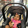 baby, car_seat, infant, pink_clothing, onesie, person, store_interior, plastic_packaging, pantyhose, glass_door, shopping, floor, seat_belt, hair_bow, black_hair, furniture, child, indoor, serious_expression, human