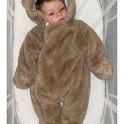 Aurora is registered to the contest to win money with this photo: baby, infant, onesie, brown, fuzzy, crib, mesh, cushion, sleepwear, child, face, person, indoors, lying_down, cozy, soft, cute, young, warm, newborn