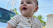 Asher is registered to the contest to win money with this photo: baby, child, infant, portrait, smiling, happy, outdoor, daylight, sky, blue_sky, striped_clothing, onesie, short_sleeves, car, parked_car, power_lines, residential_area, closeup, standing, face