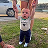 baby, child, infant, outdoor, park, grass, lakeside, adult, parent, holding_hands, standing, smiling, surprised, portrait, mickey_mouse, clothing, socks, car, trees, sunlight