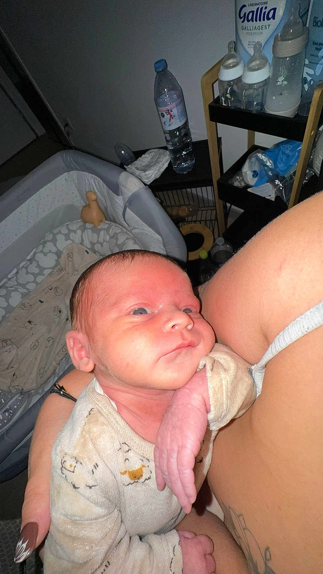 Karter a rejoint le concours — aidez-le/la à gagner de superbes lots ! baby, newborn, infant, person, arm, bottle, crib, blanket, clothing, hand, tattoo, nail_polish, baby_supplies, water_bottle, bedroom, indoor, skin, face, expression, holding