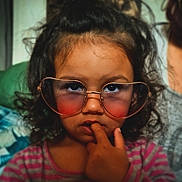 Livia participe au concours pour gagner de l'argent avec cette photo : child, curly_hair, glasses, heart_shaped_glasses, finger_in_mouth, thoughtful, portrait, indoor, pink_striped_shirt, close_up, face, person, young, casual, expression, cute, eyewear, fashion, childhood, skin
