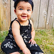 Linèa is registered to the contest to win money with this photo: baby, child, smiling, outdoor, grass, wooden_fence, headband, black_clothing, barefoot, cute, happy, sitting, portrait, young_child, summer, nature, playful, toddler, sunlight, person