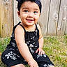 baby, child, smiling, outdoor, grass, wooden_fence, headband, black_clothing, barefoot, cute, happy, sitting, portrait, young_child, summer, nature, playful, toddler, sunlight, person
