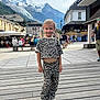 child, leopard_print, outdoor, mountain, town_square, wooden_deck, people, buildings, snow, sky, clouds, shoes, pigtails, fashion, casual, tourists, cafe, bench, daylight, smile