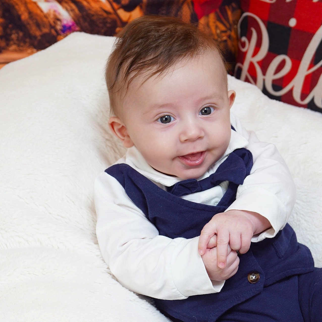 Jordan is registered to the contest to win money with this photo: baby, believe, bow_tie, child, cozy, cute, eyes, face, festive, hair, hands, indoor, infant, navy_outfit, pillow, plaid_pattern, portrait, smiling, text, white_cushion
