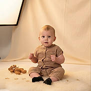 Parker is registered to the contest to win money with this photo: baby, toddler, infant, sitting, plush_rug, crocheted_toy, teddy_bear, beige_clothing, black_socks, studio_lighting, soft_light, curious_expression, indoor, portrait, child, small_stars, cozy, neutral_background, cute, young_child