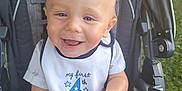 Waylon is registered to the contest to win money with this photo: baby, child, stroller, bib, smiling, happy, outdoor, grass, car_wheel, clothing, face, person, summer, celebration, cute, infant, seat, portrait, sunlight, fun