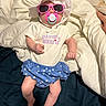 adorable, baby, bed, blanket, blue_shorts, child, clothing, cute, fashion, hat, indoor, infant, pacifier, person, pillow, relaxing, resting, sleepwear, sunglasses, white_shirt