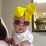 Jennalynn is registered to the contest to win money with this photo: baby, child, sunglasses, yellow_bow, white_shirt, indoor, plant, clock, person, cute, fashion, toddler, portrait, accessory, glasses, headwear, holding, adult_arm, casual, cool