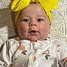baby, blanket, cheeks, child, clothing, cute, expression, eyes, face, headband, indoors, infant, lying_down, onesie, patterned_clothing, person, portrait, soft_lighting, textured_blanket, yellow_bow