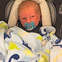 baby, pacifier, blanket, car_seat, dinosaur_pattern, infant, child, sleepy, cozy, soft, blue, yellow, green, striped_headrest, comfort, cute, indoors, young_child, face, resting
