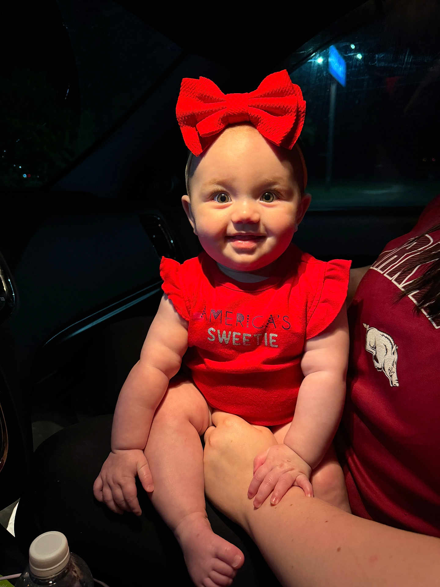 Briar joined the competition — help win amazing prizes! baby, child, red_bow, red_clothing, smile, indoor, car_interior, night, adult_hand, holding, cute, portrait, chubby_cheeks, headband, person, happy, eyes, face, infant, sitting