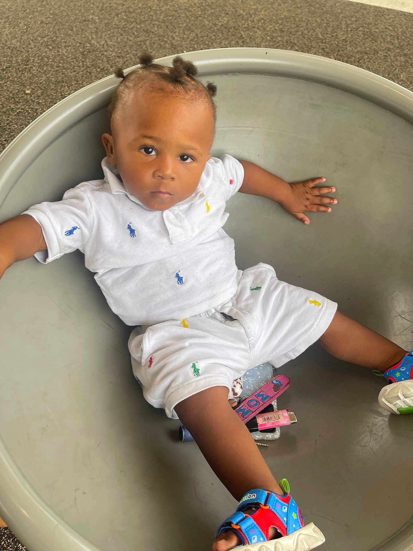 Lamont joined the competition — help win amazing prizes! toddler, child, white_clothing, colorful_logos, sandals, hair_buns, round_container, floor, indoor, curious_expression, small_objects, casual_outfit, childrens_fashion, skin, person, portrait, sitting, young_child, play_area, comfortable