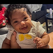 Lyric joined the competition — help win amazing prizes! baby, child, smiling, curly_hair, shirt, lemon, hand, person, indoor, couch, table, living_room, happy, cute, infant, portrait, clothing, human, face, sitting