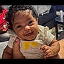 baby, child, smiling, curly_hair, shirt, lemon, hand, person, indoor, couch, table, living_room, happy, cute, infant, portrait, clothing, human, face, sitting