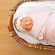 Lennon is registered to the contest to win money with this photo: newborn, baby, sleeping, swaddled, pink, headband, basket, woven, wooden_floor, infant, peaceful, cozy, cute, portrait, child, resting, soft, indoors, blanket, adorable