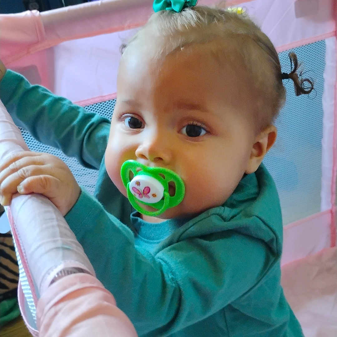 Xai'Lynn joined the competition — help win amazing prizes! toddler, child, pacifier, playpen, pink, teal_shirt, pigtails, indoor, toy_box, cartoon, curious, baby, face, hand, standing, furniture, colorful, young_child, expression, hair