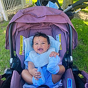 Haanvika is registered to the contest to win money with this photo: baby, baby_carrier, blue_socks, child, clothing, cute, daylight, grass, happy, infant, nature, outdoor, person, playful, purple, seat_belt, smiling, stroller, sunlight, tree