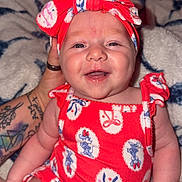Wrenlee Jade is registered to the contest to win money with this photo: baby, smiling, red_outfit, headband, tattoo, hand, blanket, pattern, happy, infant, cute, portrait, indoor, person, skin, sitting, clothing, face, child, young