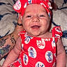 baby, smiling, red_outfit, headband, tattoo, hand, blanket, pattern, happy, infant, cute, portrait, indoor, person, skin, sitting, clothing, face, child, young