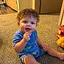 Jayce joined the competition — help win amazing prizes! toddler, child, curly_hair, blue_clothing, carpet, indoor, toy, floor, door, wooden_door, happy, sitting, person, playful, cute, baby, smiling, hand, furniture, room