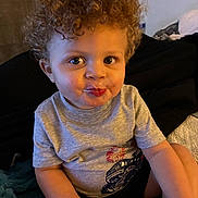 Jayce joined the competition — help win amazing prizes! toddler, child, curly_hair, indoor, grey_tshirt, pout, sitting, blanket, cushion, face, person, cute, expression, young_child, skin, arm, eyes, hair, clothing, casual