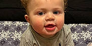 Jayce joined the competition — help win amazing prizes! baby, child, curly_hair, blue_eyes, gray_shirt, diaper, blanket, patterned_blanket, indoor, furniture, laundry_basket, floor, cute, smiling, portrait, sitting, hands, face, young_child, home