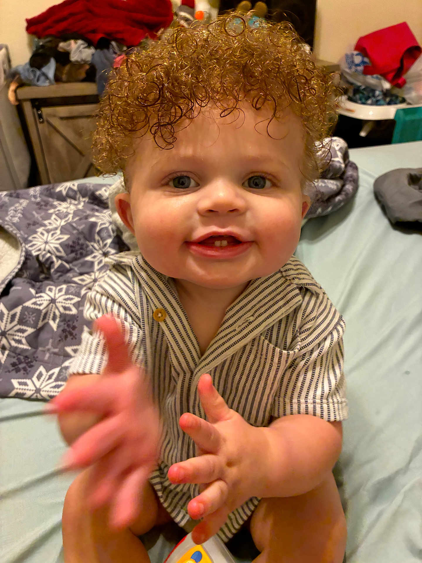 Jayce joined the competition — help win amazing prizes! baby, child, curly_hair, smiling, happy, sitting, indoor, bed, blanket, clothing, striped_shirt, hand, face, person, cute, infant, room, toy, skin, young