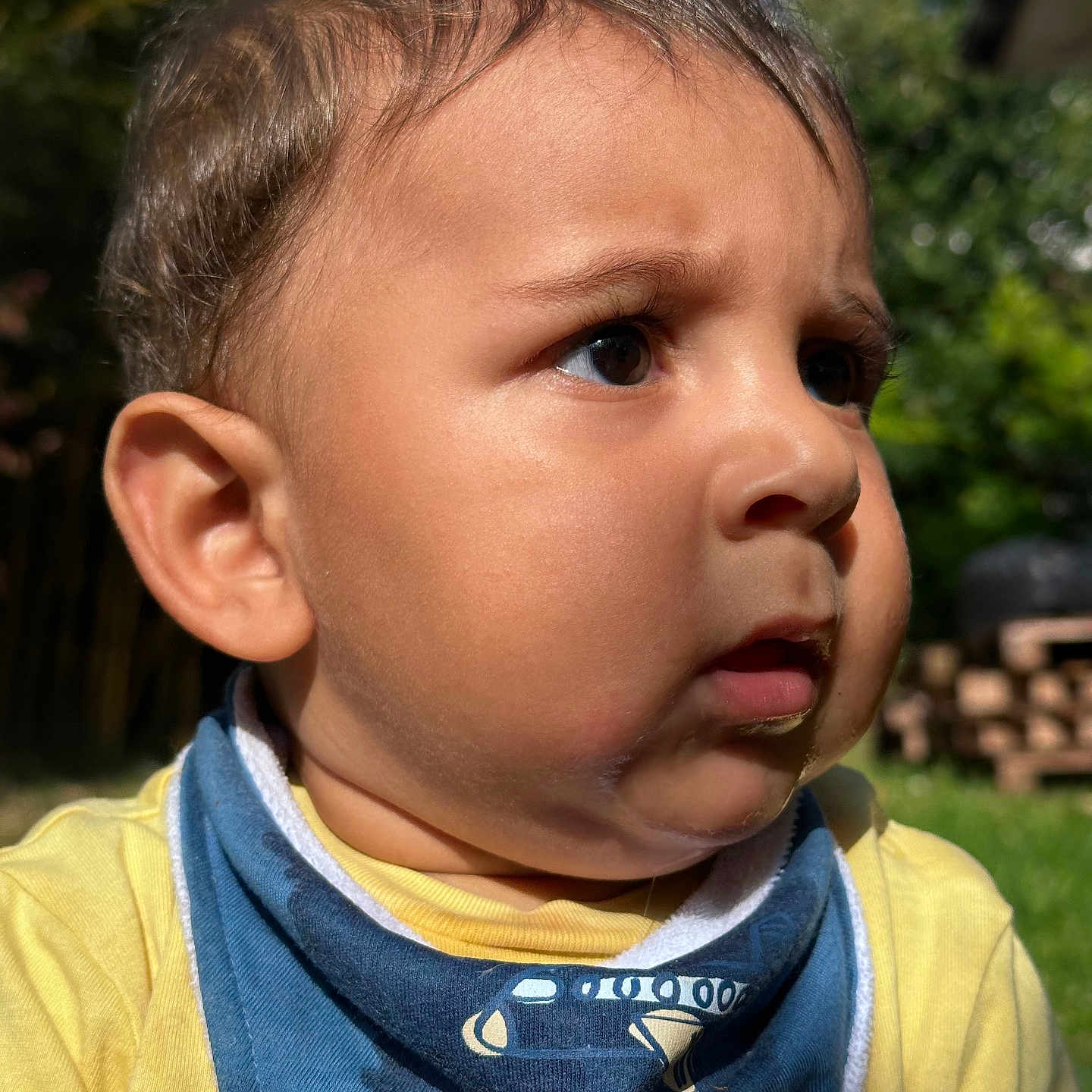 Donato participe au concours pour gagner de l'argent avec cette photo : baby, child, face, outdoor, sunlight, yellow_shirt, blue_bib, portrait, curious, expression, cheeks, skin, hair, person, nature, greenery, daylight, closeup, young, infant