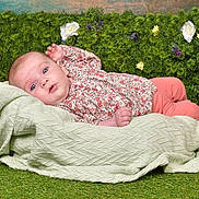 Emma a rejoint le concours — aidez-le/la à gagner de superbes lots ! baby, infant, blanket, greenery, flowers, grass, portrait, blue_eyes, floral_clothing, pink_pants, cute, lying_down, soft_texture, nature_background, indoors, child, person, face, skin, curious