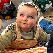 Emma a rejoint le concours — aidez-le/la à gagner de superbes lots ! baby, blanket, blue_eyes, candy_cane, child, christmas_tree, curious, cute, festive, floor, headband, holiday, holiday_decor, indoors, infant, overalls, penguin_decoration, portrait, smiling, toddler