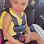 toddler, child, car_seat, yellow_bow, yellow_clothing, smiling, happy, seatbelt, car_interior, heart_pattern, safety, cute, baby, young_child, portrait, sunlight, seat, hands, face, curly_hair