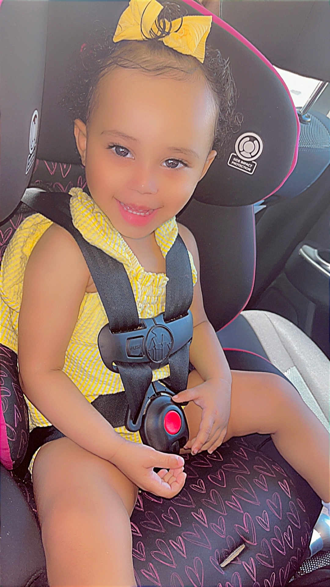 Te'Niyah joined the competition — help win amazing prizes! toddler, child, car_seat, yellow_bow, yellow_clothing, smiling, happy, seatbelt, car_interior, heart_pattern, safety, cute, baby, young_child, portrait, sunlight, seat, hands, face, curly_hair