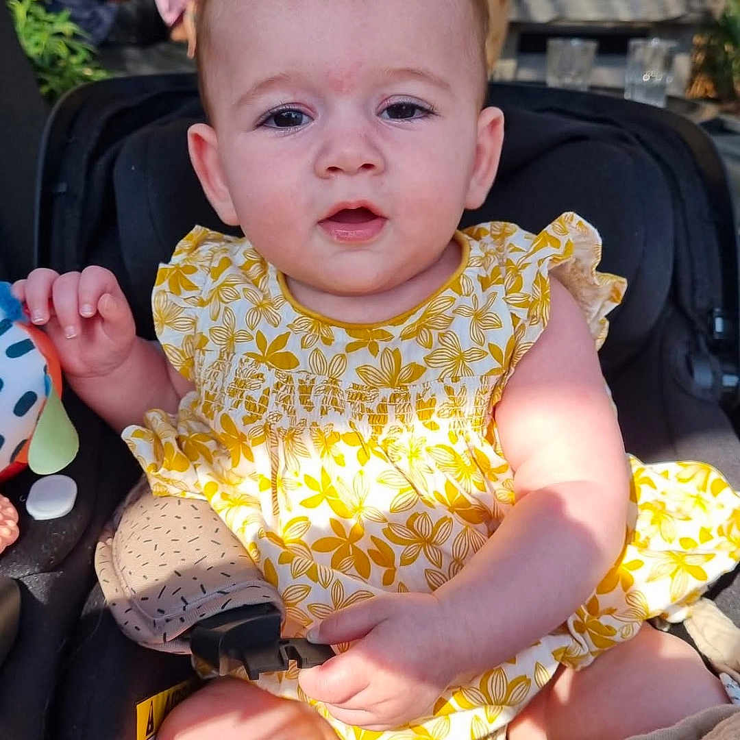 Ellvyra participe au concours pour gagner de l'argent avec cette photo : baby, blurred_background, cafe, car_seat, casual, child, curious_expression, cute, daylight, infant, outdoor, people, person, portrait, seatbelt, smile, summer_clothing, sunlight, toy, yellow_dress