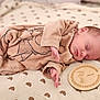 baby, newborn, sleeping, onesie, blanket, pattern, wooden_marker, milestone, peaceful, infant, cute, soft, cozy, child, portrait, indoors, resting, clothing, hand, face