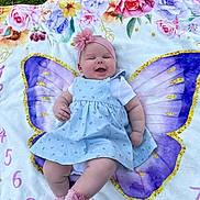 Eliana joined the competition — help win amazing prizes! baby, infant, blanket, butterfly_wings, headband, flower, smile, dress, socks, grass, outdoor, milestone_blanket, floral_pattern, chubby_legs, portrait, lying_down, pink, purple, happy, cute