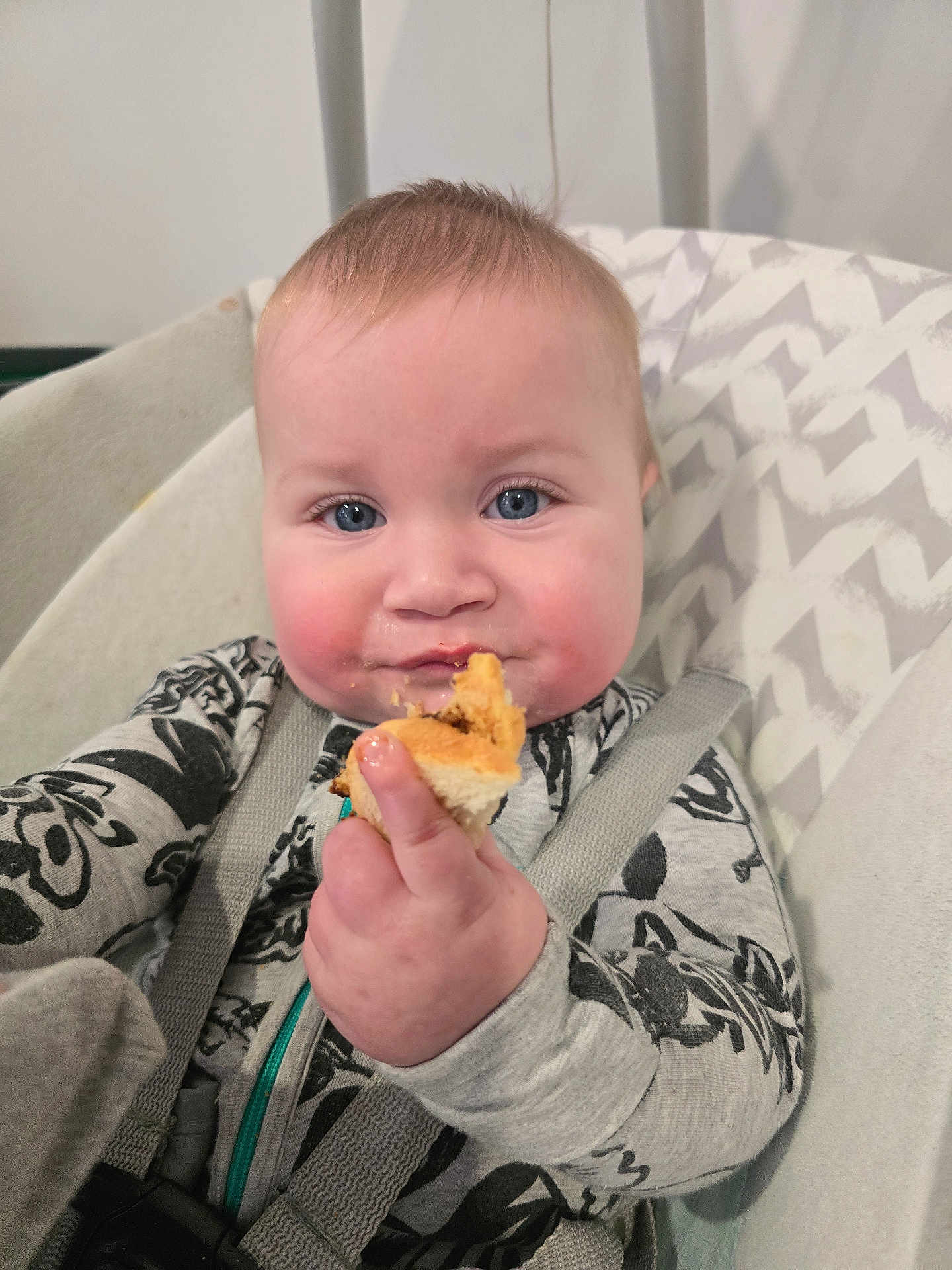 Declyn is registered to the contest to win money with this photo: baby, child, food, bread, high_chair, face, blue_eyes, hand, clothing, pattern, cushion, seatbelt, indoor, cute, portrait, infant, skin, smile, young, person