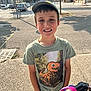 baseball_cap, boy, casual_clothing, child, daylight, hands_in_pockets, happy, nature, outdoor, parking_lot, person, portrait, sidewalk, smiling, stroller, sunny, trees, tshirt, urban, young_person