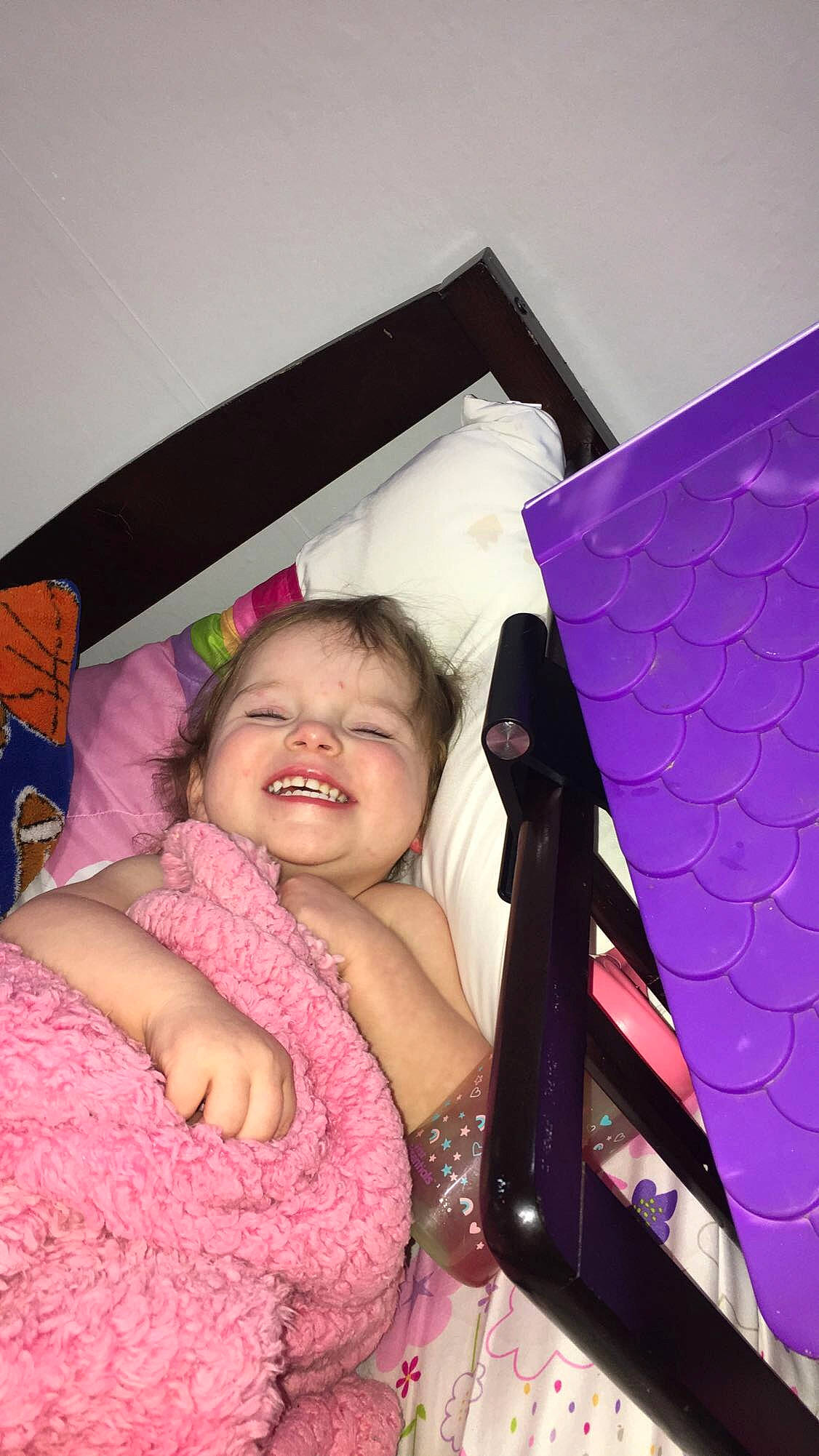 Loretta is registered to the contest to win money with this photo: baby, baby_toddler_clothing, bed, car_seat, child, comfort, event, finger, fun, happy, joy, linens, magenta, pattern, person, pink, purple, room, sitting, smile