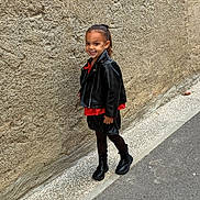 Tya a rejoint le concours — aidez-le/la à gagner de superbes lots ! child, smiling, leather_jacket, red_top, black_skirt, black_boots, street, sidewalk, wall, urban, fashion, posing, happy, person, young, outdoor, confident, casual, footwear, hair_tied_back