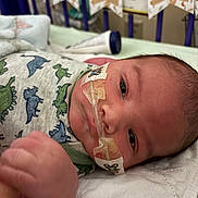 Leonardo is registered to the contest to win money with this photo: newborn, baby, infant, child, face, eyes, hospital, medical, medical_tape, swaddle, blanket, dinosaur_pattern, bed, bedding, portrait, close_up, lying_down, indoor, healthcare, wide_eyed