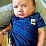 Ace joined the competition — help win amazing prizes! baby, infant, child, blue_shirt, beige_shorts, cushion, gray_cushion, indoor, person, face, expression, sitting, hand, hair, skin, clothing, looking, young_child, cute, portrait