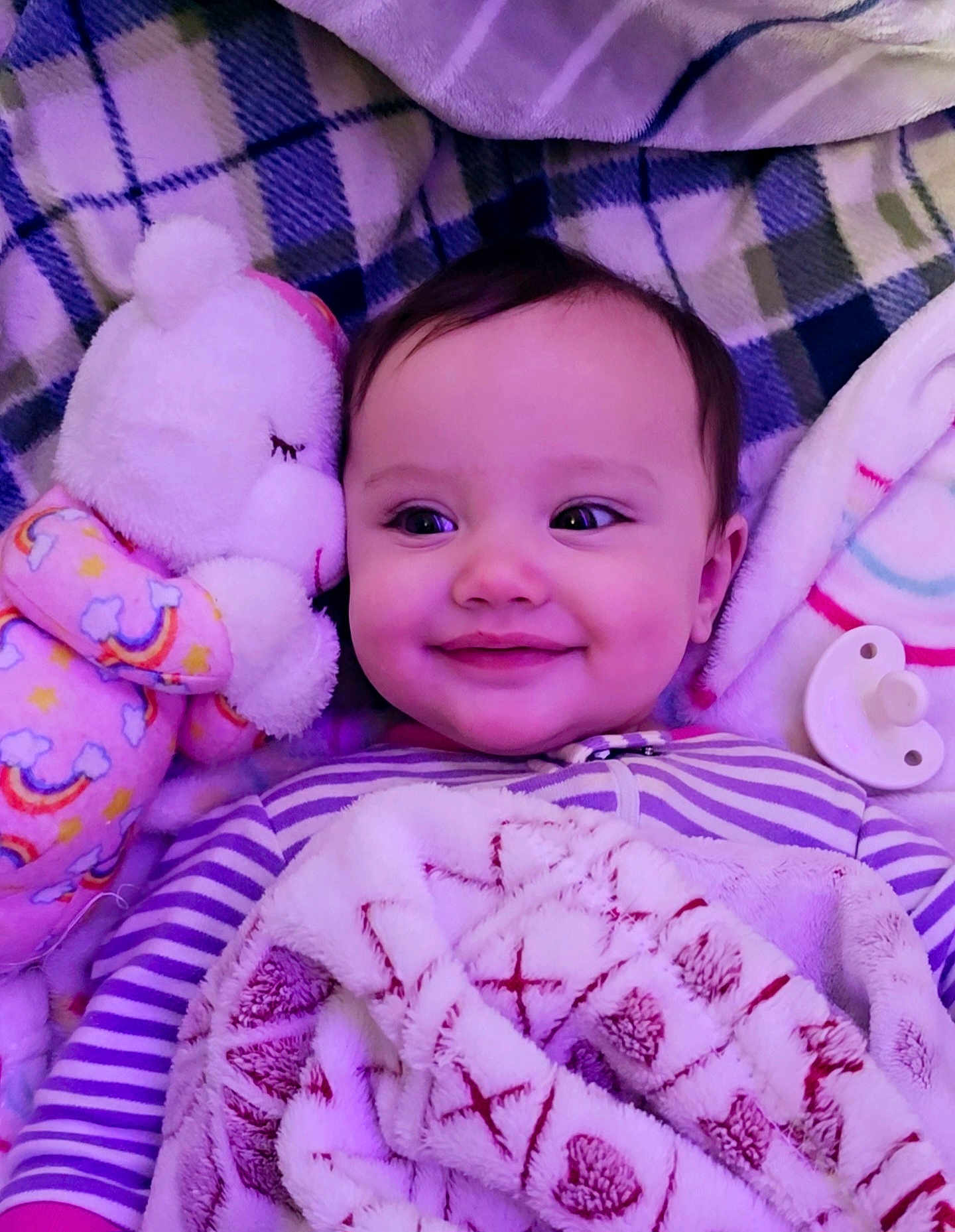 Ember is registered to the contest to win money with this photo: baby, smiling, blanket, plush_toy, pacifier, striped_clothing, face, child, infant, cozy, soft_toys, purple_lighting, lying_down, cute, happy, indoors, portrait, warm, comfort, head