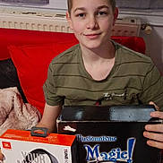 Leny a rejoint le concours — aidez-le/la à gagner de superbes lots ! box, boy, casual_clothing, child, couch, curtains, gift, headphones, indoor, jbl, magic_kit, person, present, radiator, red_couch, seated, short_hair, smiling, technology, window