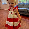 Kleo is registered to the contest to win money with this photo: child, toddler, baby, portrait, smiling, standing, dress, strawberry, red_clothing, cream_clothing, barefoot, indoors, living_room, couch, wood_floor, window, daylight, home, fashion, happy